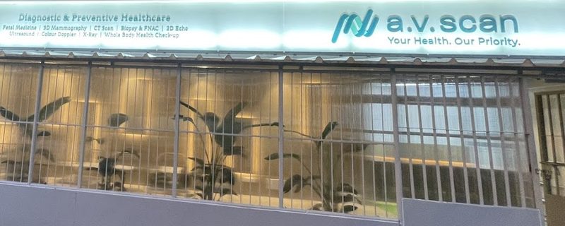 The lit a.v.scan signboard above the ground-floor entrance of AV Scan Diagnostics in Dadar West, seen from the pavement
