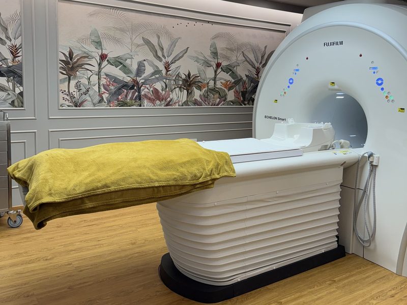 MRI room at AV Scan Diagnostics: the wide-bore scanner, its padded table with a folded blanket, and a botanical mural behind